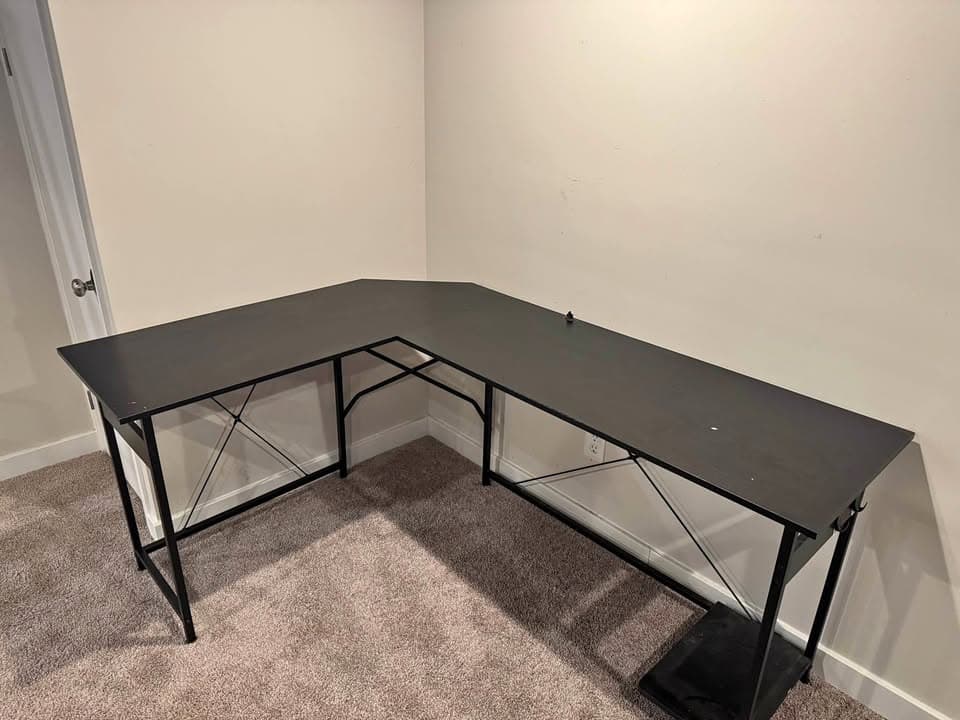 Black L-shaped corner desk with a metal frame in an empty room