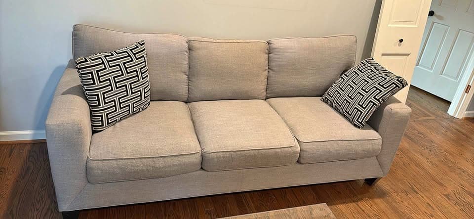 Light gray three-seat fabric sofa with two patterned throw pillows